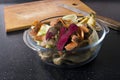 Closeup of glass bowl full of leftover vegetables peelings, wooden cutting board and knife on the black kitchen table.Concept of z