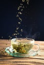 Closeup of glass cup of hot green tea on wooden table with dry tea leaves falling into the cup Royalty Free Stock Photo