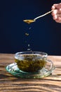 Closeup of glass cup of hot green tea on wooden table with a teaspoon in a hand with falling tea drops