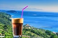 Closeup of a glass of iced coffee on background of a beautiful view of the Aegean sea