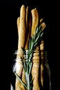 Glass jar full of Italian grossing with green rosemary herb on a black background