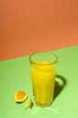 Vertical image.Glass of fresh sweet orange juice and slice of orange on the green surface against bright orange background.Empty s Royalty Free Stock Photo