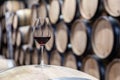 Closeup glass with red wine on background wooden wine oak barrel stacked in straight rows in order, old cellar of winery, vault.