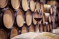 Closeup glass with red wine on background wooden wine oak barrel stacked in straight rows in order, old cellar of winery, vault. Royalty Free Stock Photo