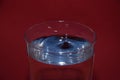 Closeup of glass of water with blue reflection on it, with a splashing droplet on a red background