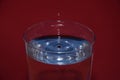 Closeup of glass of water with blue reflection on it, with a splashing droplet on a red background