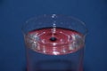 Closeup of glass of water with red reflection on it, with a splashing droplet on a blue background