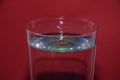 Closeup of a glass of water with a splashing droplet on a red background