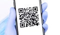 Gloved hand holding a smartphone with qr code on the screen. Stopcoronavirus.rf - website you can find detailed