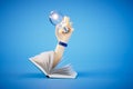 Closeup glowing light bulb in the hand and book on a blue background. 3d render