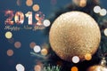 Closeup of gold bauble hanging from a decorated Christmas tree. Shiny happy new year concept with 2019 happy new year text