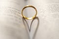 Closeup of a golden engagement ring forming a shadow of a heart on the open holy bible Royalty Free Stock Photo