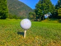 Closeup of a golf ball on a tee on the grass surrounded by mountains under the sunlight Royalty Free Stock Photo