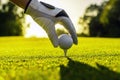 Hand of golfer wearing glove placing golf ball on a tee at golf course with sunlight on background