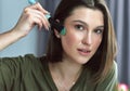 Closeup of a gorgeous brunette young woman looking directly to the camera and making makeup herself with a brush. Attractive Royalty Free Stock Photo