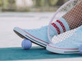 Closeup ground level shot of white sneakers with a ball under them and a racket next to them