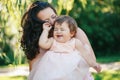 Closeup group portrait of beautiful white Caucasian brunette mother holding laughing baby daughter kissing her in cheek Royalty Free Stock Photo