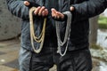 Closeup of a guy in black grungy outfit, holding silver and golden chains