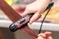 Closeup of hairdresser hands with styling iron straightening woman hair in salon.