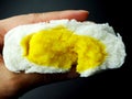 Closeup half inside of yellow custard cream bun in hand fingers on black background