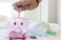 Closeup,hand of Asian child girl put coin through the hole in pink piggy bank with medical protective mask,saving money for health Royalty Free Stock Photo