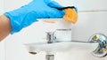 Closeup of hand in blue rubber glove washing and cleaning shiny metal water tap in bathroom while doing housework and Royalty Free Stock Photo