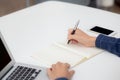 Closeup hand of business man writing on note while using laptop computer on desk at home. Royalty Free Stock Photo