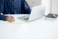 Closeup hand of business man writing on note while using laptop computer on desk at home. Royalty Free Stock Photo