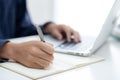 Closeup hand of business man writing on note while using laptop computer on desk at home. Royalty Free Stock Photo