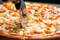 Closeup hand of chef baker in white uniform cutting pizza at kitchen Royalty Free Stock Photo