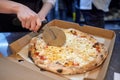 Closeup hand of chef baker in white uniform cutting pizza at kitchen. Royalty Free Stock Photo