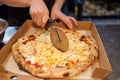 Closeup hand of chef baker in white uniform cutting pizza at kitchen. Royalty Free Stock Photo