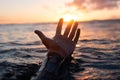 Closeup of a hand coming out of the water on the background of a golden sunset reflected on the sea Royalty Free Stock Photo