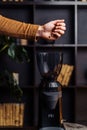 Closeup of the hand of a girl who pours out coffee beans into a black, stylish coffee grinder. Coffee beans slowly fall into the