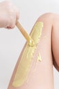 Closeup hand in glove applying hot wax on woman leg using spatula. Professional depilation procedure