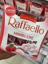 Closeup of hand holding box with Ferrero Raffaello raspberry sweets in front of shelf in german supermarket