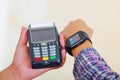 Closeup hand holding credit card payment terminal, another arm wearing smart watch with screen lit, white studio Royalty Free Stock Photo