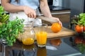 Closeup hand holding knife cutting orange fruit on a wooden chop board. Jar with mixed fruit juice  and glass bowl with a variety Royalty Free Stock Photo