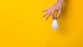 Closeup hand holding white led lighting bulb against a yellow wide background banner with copyspace. concept of idea, energy and Royalty Free Stock Photo