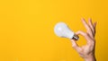 Closeup hand holding white led lighting bulb against a yellow wide background banner with copyspace. concept of idea, energy and Royalty Free Stock Photo
