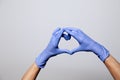 Closeup of a hand in latex rubber medical purple gloves folded into a heart sign. Isolated on white background. Concept love Royalty Free Stock Photo