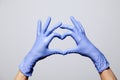 Closeup of a hand in latex rubber medical purple gloves folded into a heart sign. Isolated on white background. Concept love Royalty Free Stock Photo