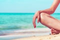 Closeup hand and leg of woman sit on sand beach at seaside. Happy young Asian woman relax and enjoy holiday at tropical paradise