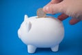 Hand of man putting euro coin in white piggy bank on blue background Royalty Free Stock Photo