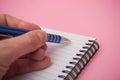 hand of man writing with blue pen on spirales note book on pink background Royalty Free Stock Photo