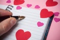 hand of man writing with vintage pen on spirales note book with paper hearts on pink background Royalty Free Stock Photo