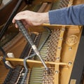 Hand and tools of tuner working on grand piano