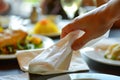 closeup of a hand unfolding a paper napkin with a meal in the background