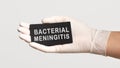 Closeup of the hand in a white sterile glove holding a card with words - Bacterial Meningitis