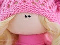Closeup of a handmade textile doll face with blond hair and knitted clothes